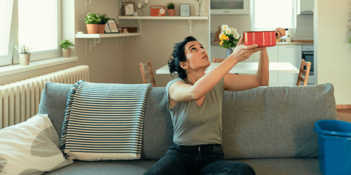 Woman holding a pot to catch leaking water from home's roof